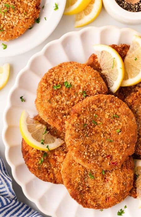 Overhead shot of crispy salmon cakes garnished with parsley and lemon wedges on a white serving platter, with black pepper and extra salmon cakes in the background