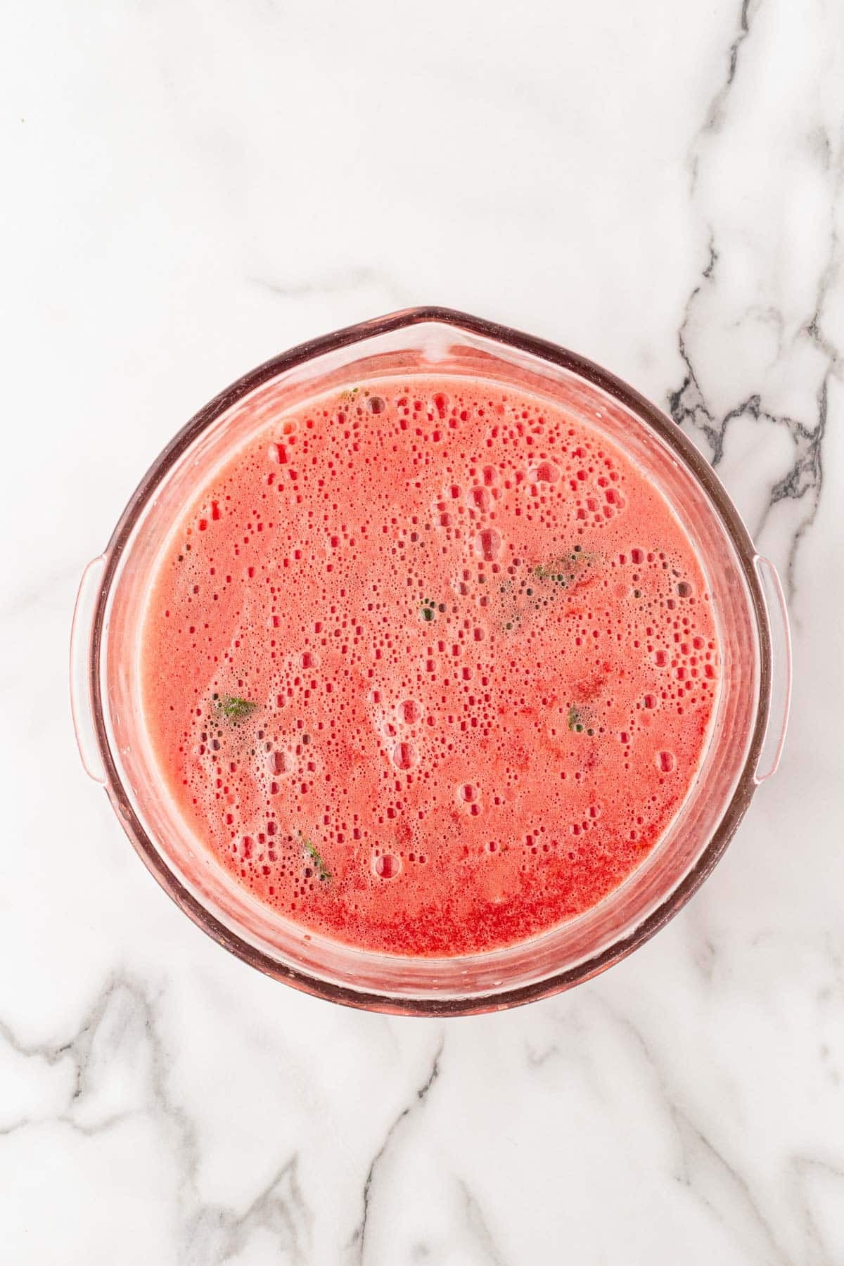 Watermelon puree mixed with the lemon and mint mixture in a large bowl on a white marble countertop