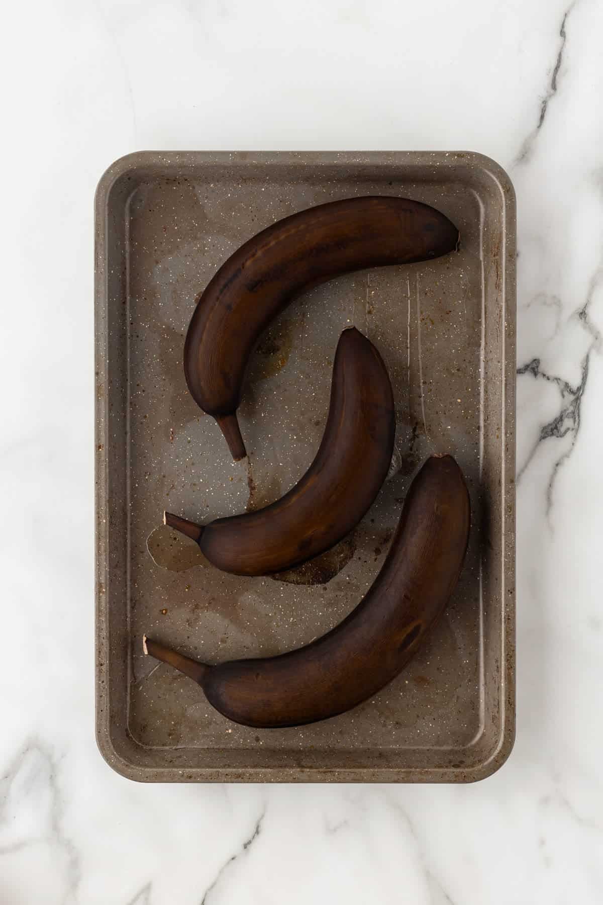 Roasted bananas with blackened peels on a baking sheet