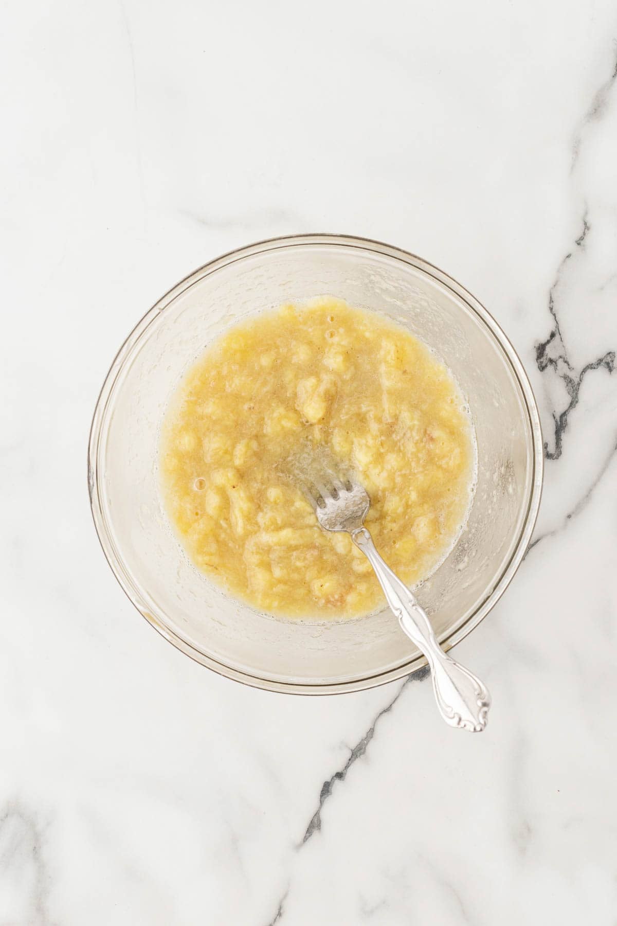 Mashed roasted bananas in a glass bowl with a fork