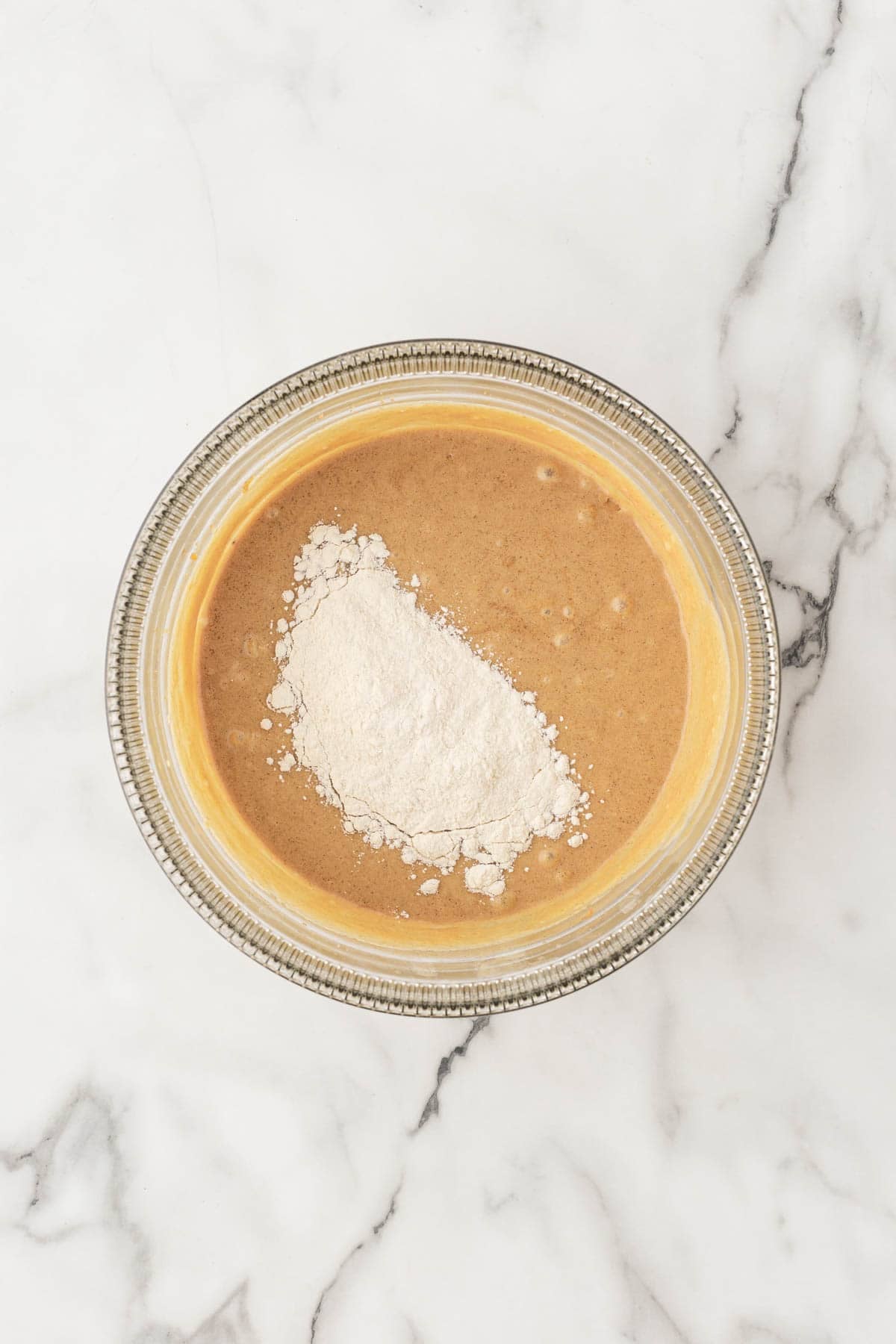 Flour mixture added to the banana muffin batter in a glass bowl