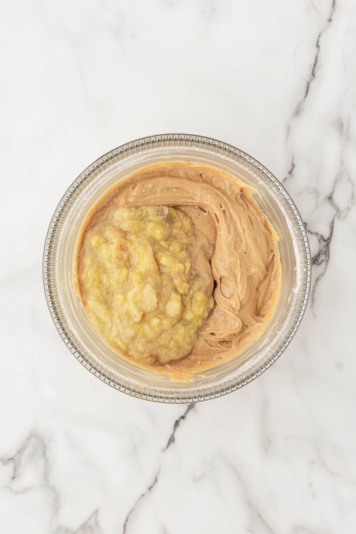 Mashed roasted bananas added to a bowl of creamed butter and brown sugar
