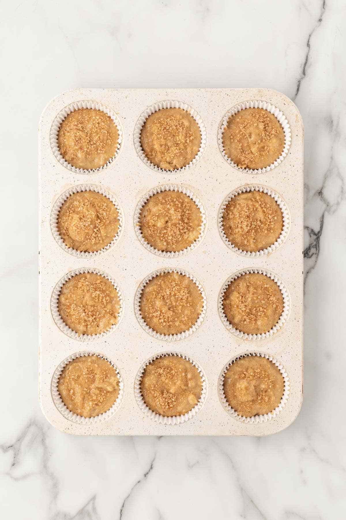 Banana muffin batter portioned into a lined muffin pan and topped with turbinado sugar