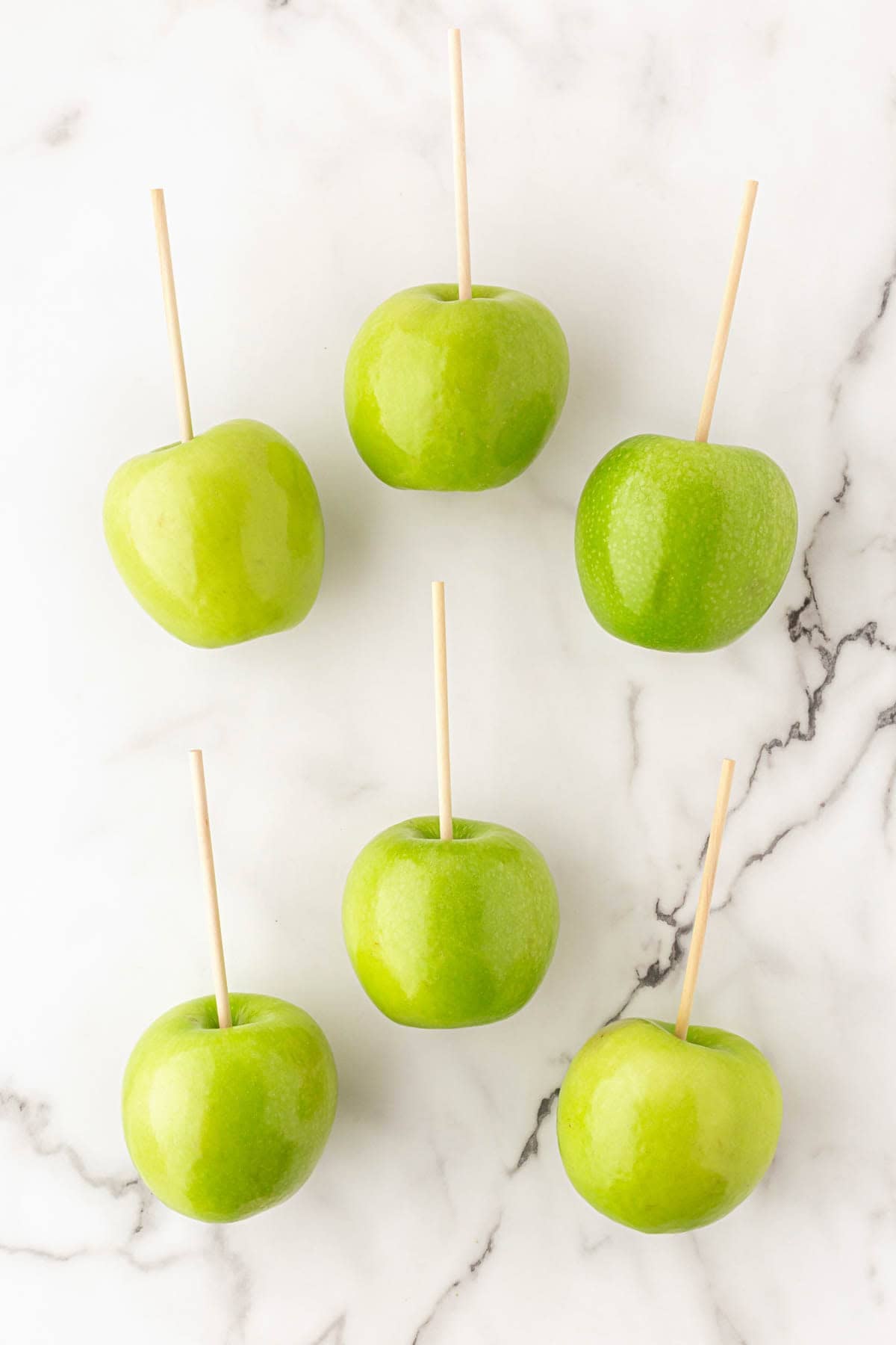 Six green apples with wooden sticks inserted into the centers