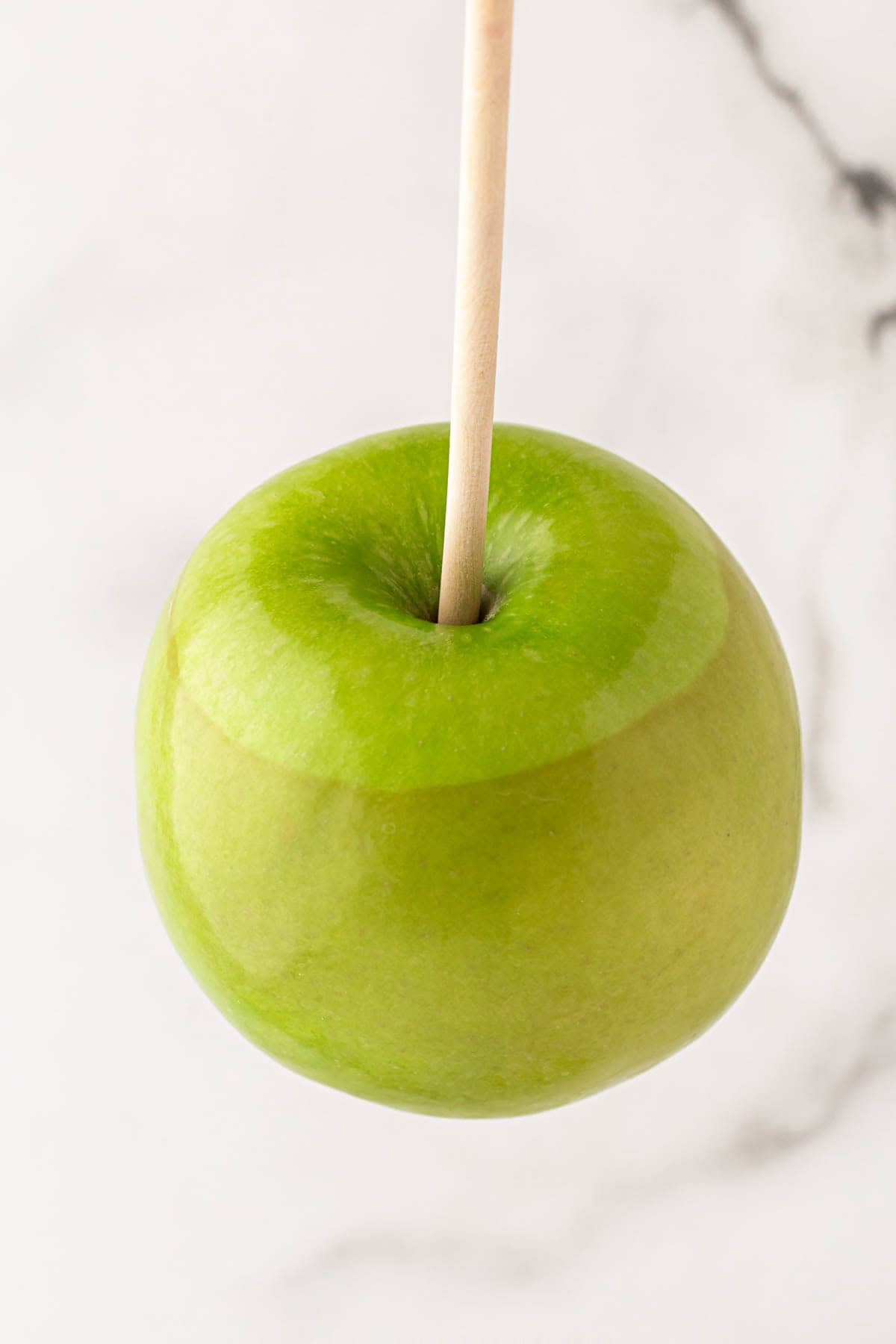 Blanched green apple with a wooden stick showing a slight color change after boiling