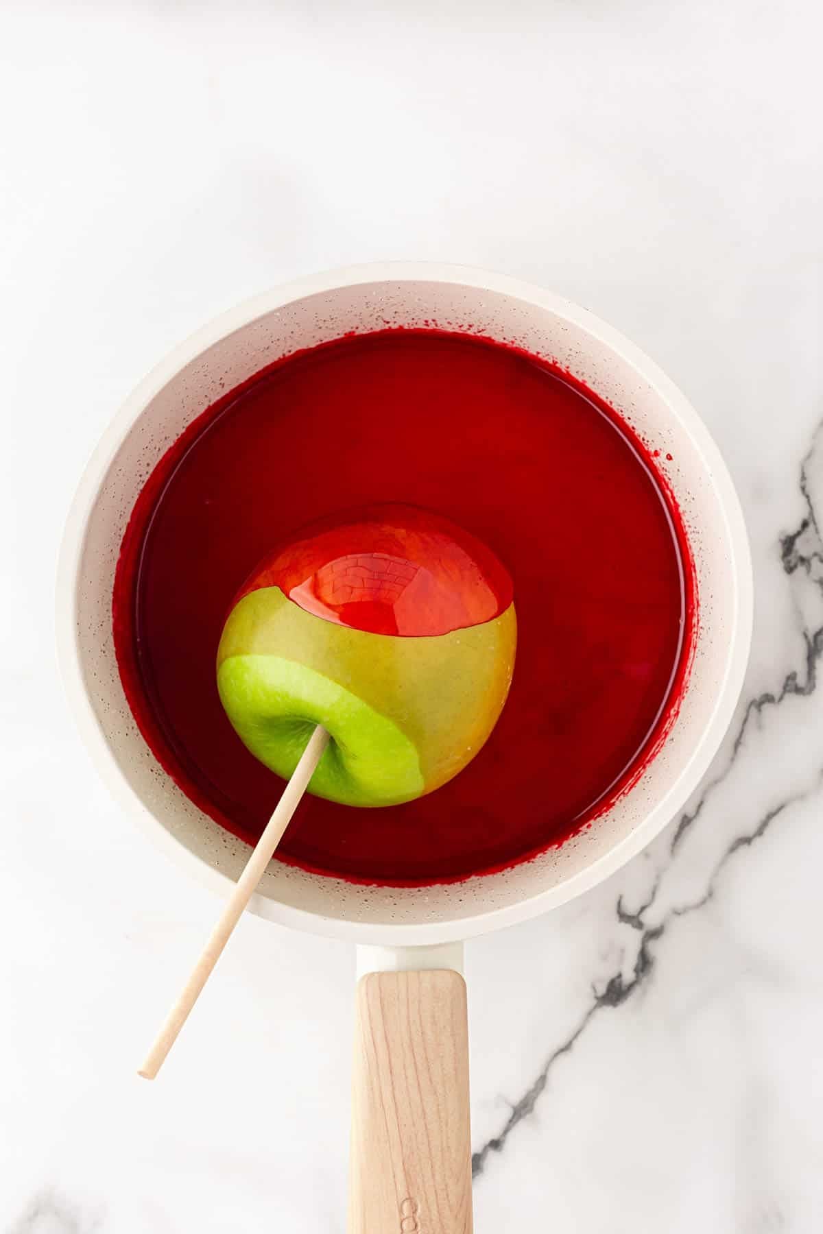 Green apple on a wooden stick being dipped into red candy coating