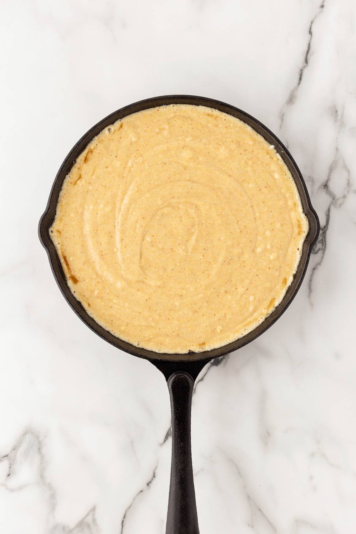 Honey butter cornbread batter spread in a cast iron skillet