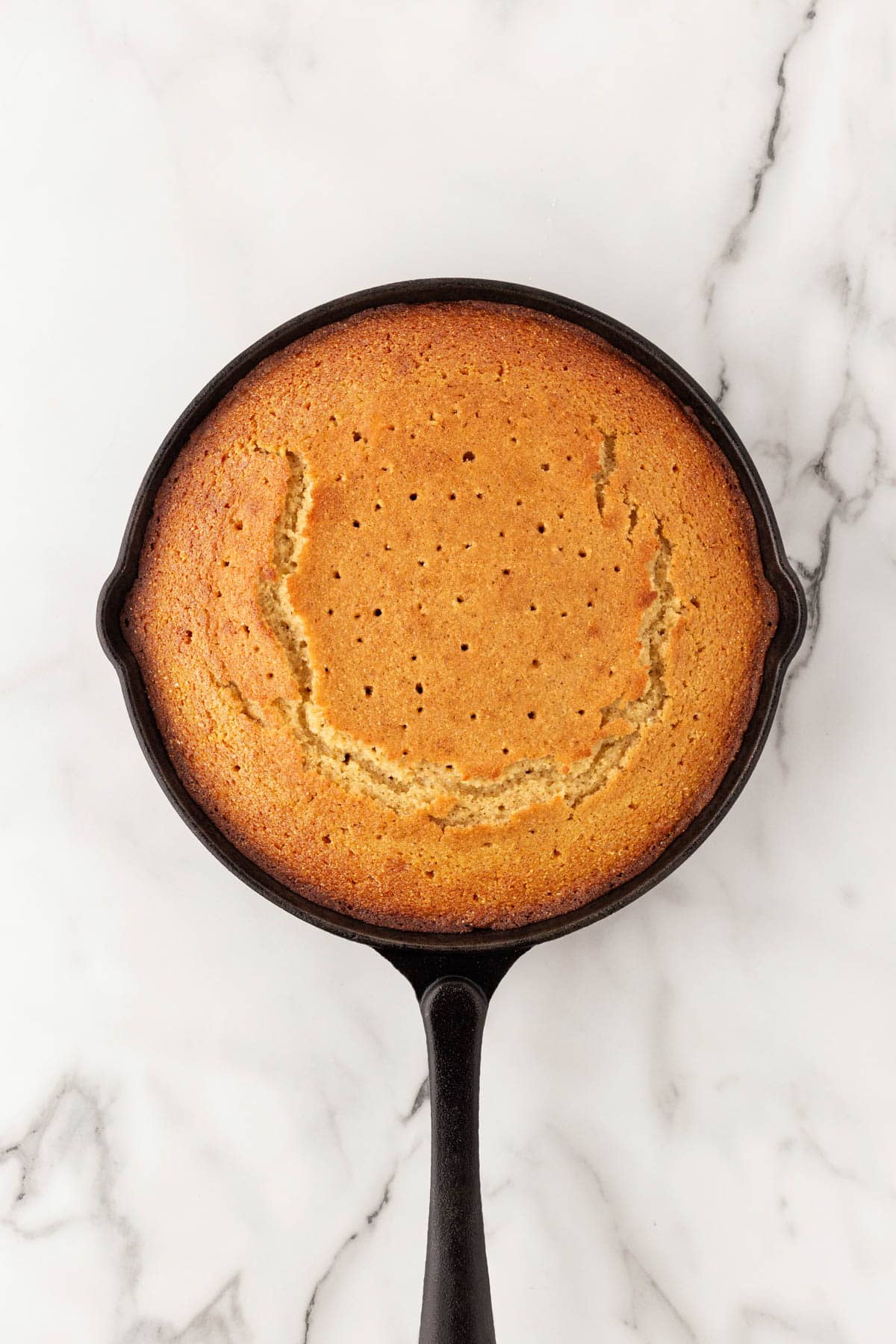 Freshly baked honey butter cornbread with holes poked in the top in a cast iron skillet