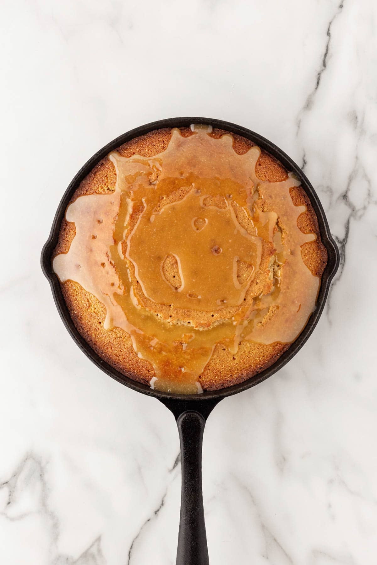 Honey butter glaze poured over warm cornbread in a cast iron skillet