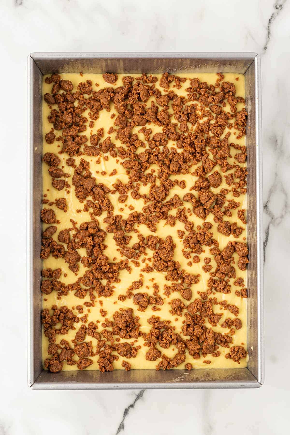 Biscoff crumble layered over cake batter in a baking pan