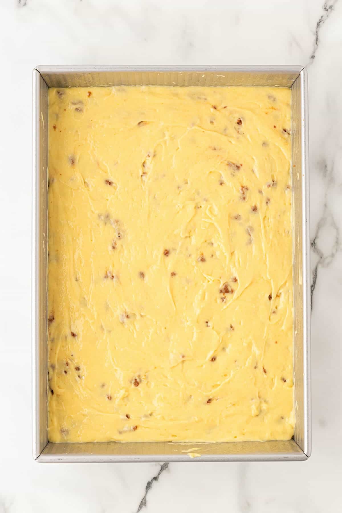 Cake batter spread over the Biscoff crumble layer in a baking pan