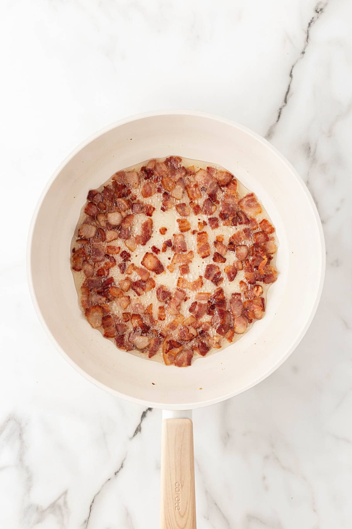 Chopped bacon cooking in a skillet until crisp and the fat renders