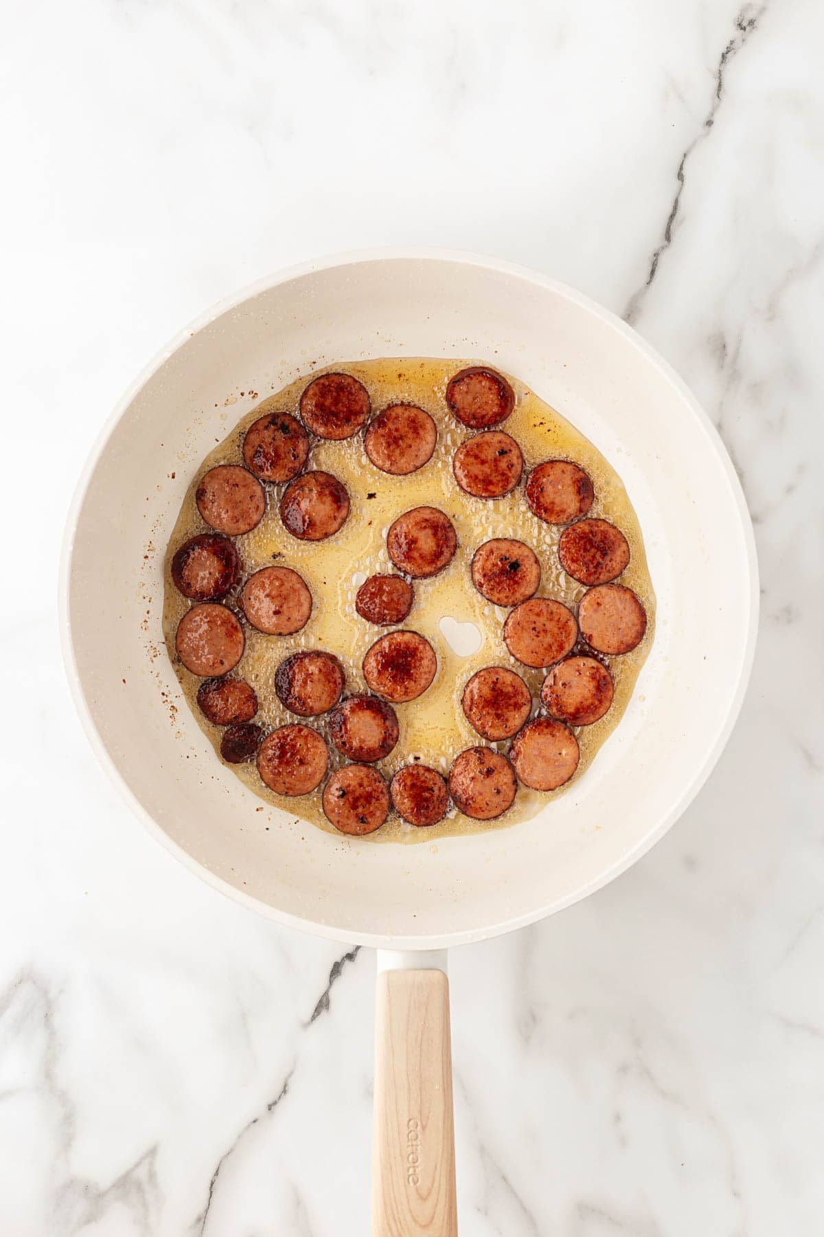 Sliced andouille sausage browning in rendered bacon fat in a skillet