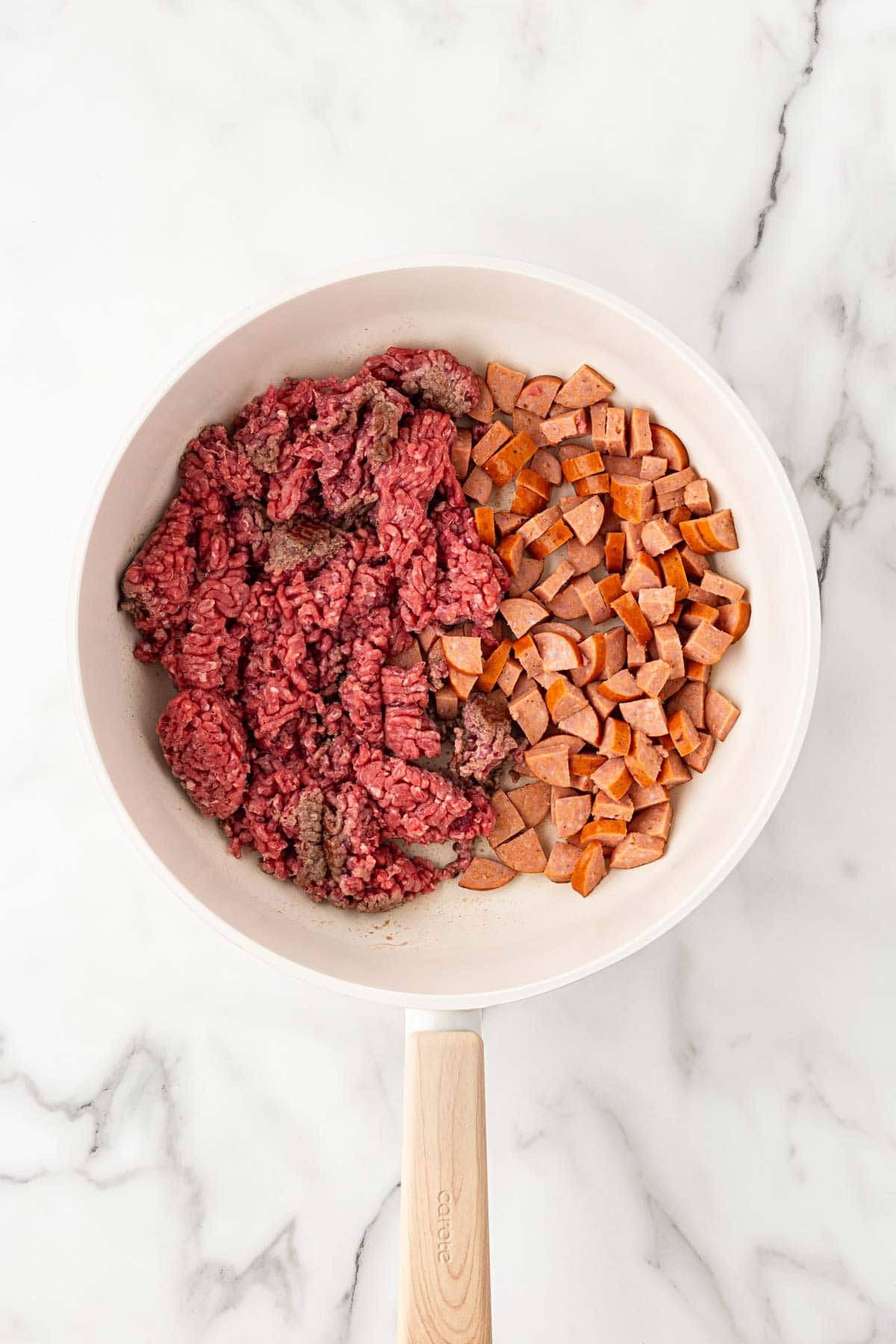 Ground beef and diced andouille sausage cooking together in a large skillet