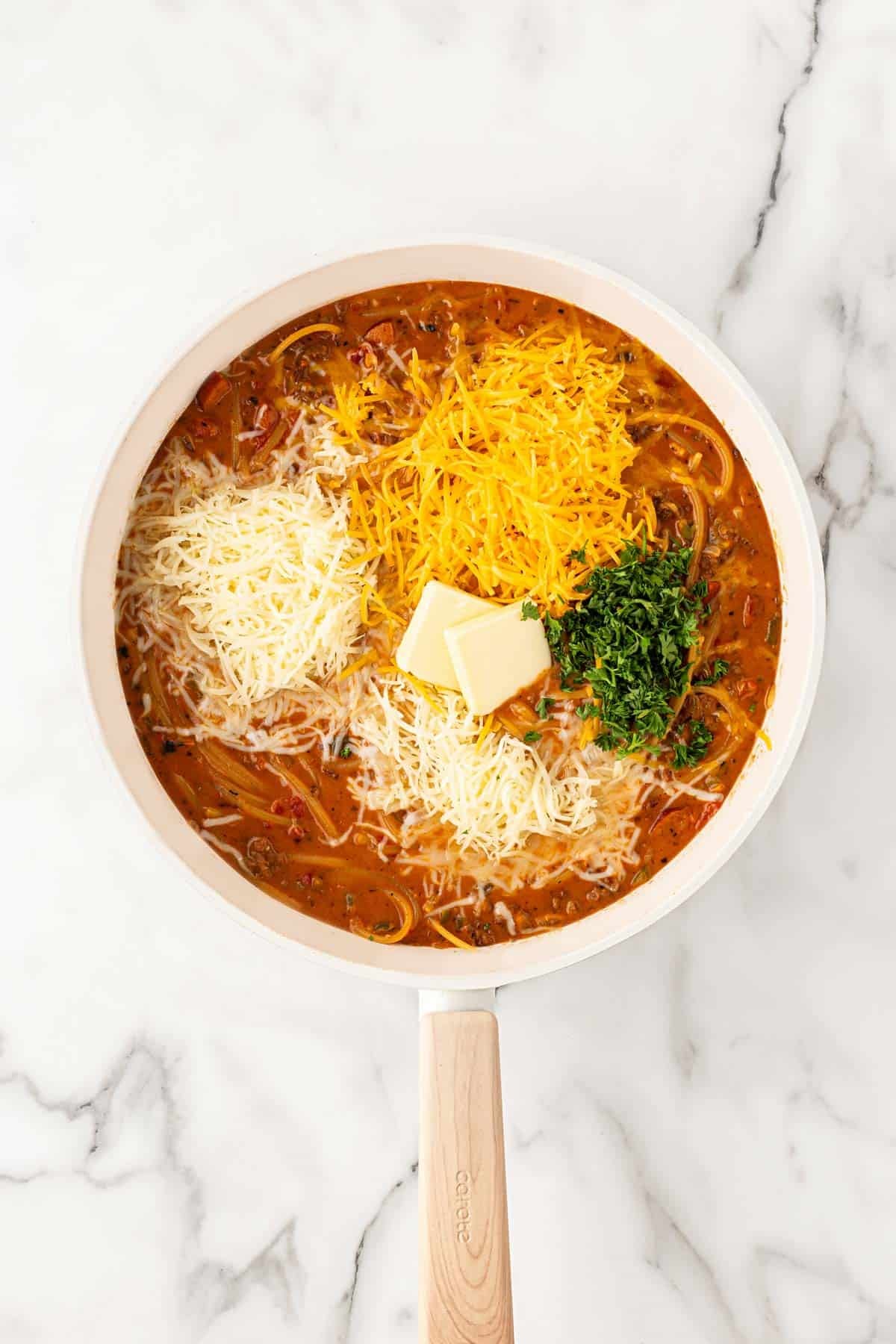Cooked spaghetti and meat sauce topped with shredded cheeses, butter, and chopped parsley