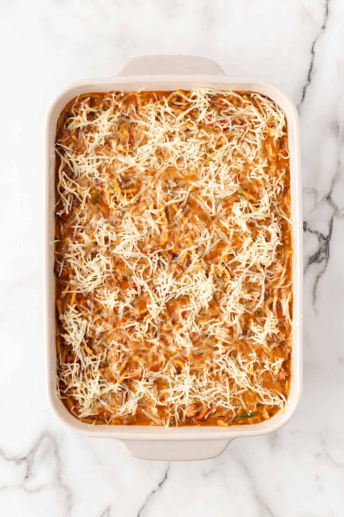 Dirty spaghetti topped with shredded mozzarella in a baking dish before baking