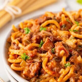 Closeup of baked dirty spaghetti with beef, andouille sausage, melted cheese, and parsley