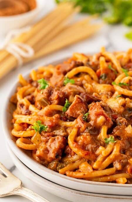 Closeup of baked dirty spaghetti with beef, andouille sausage, melted cheese, and parsley