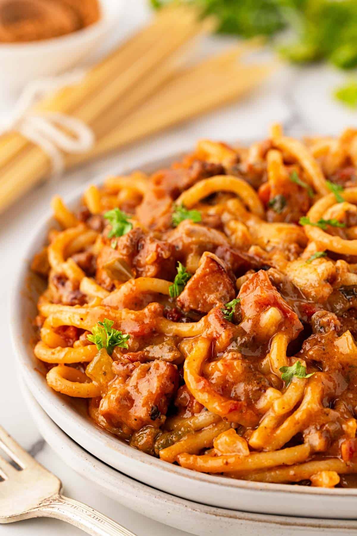 Closeup of baked dirty spaghetti with beef, andouille sausage, melted cheese, and parsley