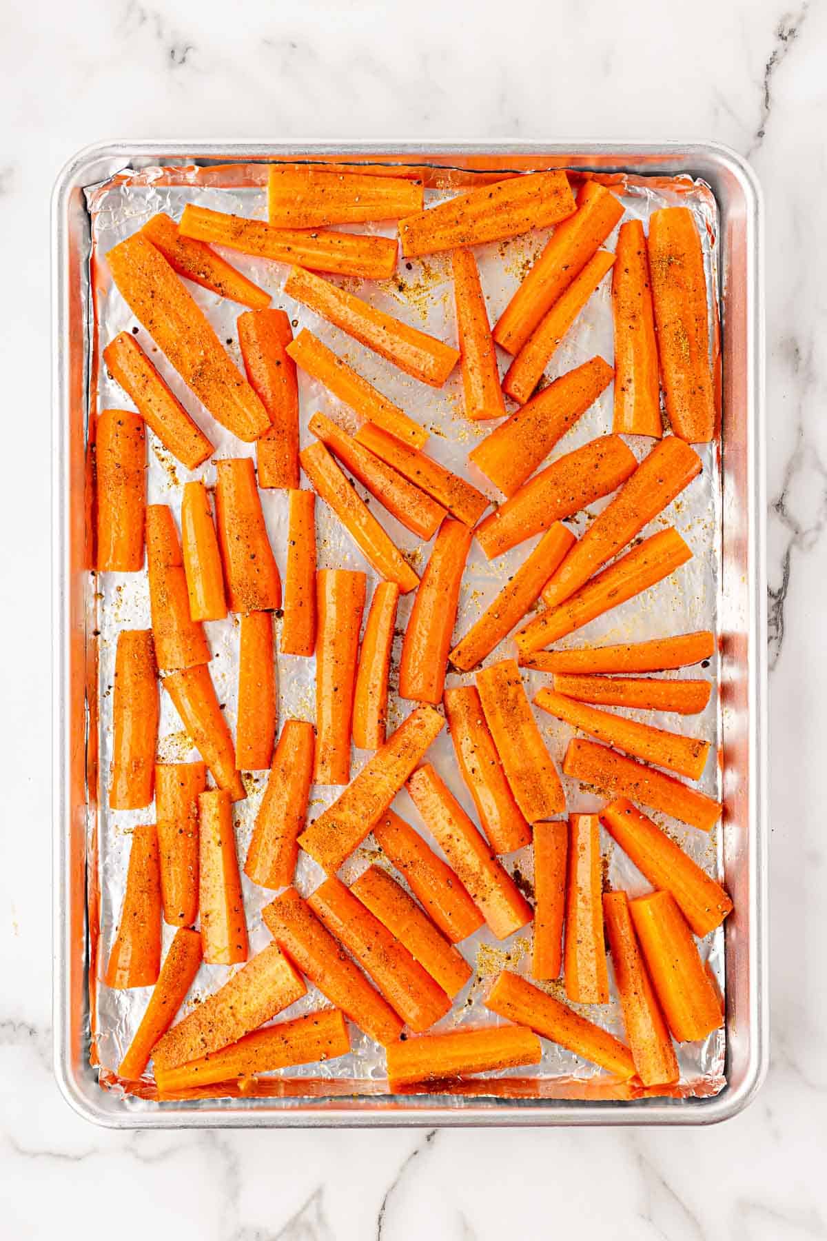 Carrot pieces seasoned with curry and Cajun seasoning on a foil-lined baking sheet