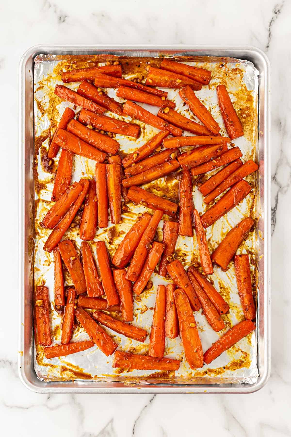Tender roasted carrots coated in peanut maple sauce on a baking sheet