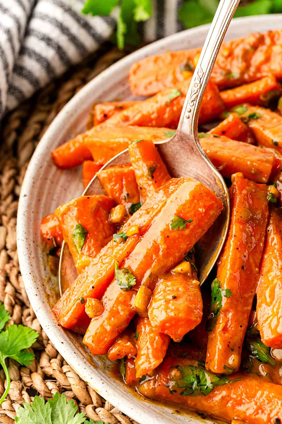 Closeup of a spoon lifting roasted carrots coated in peanut maple sauce with chopped peanuts and cilantro