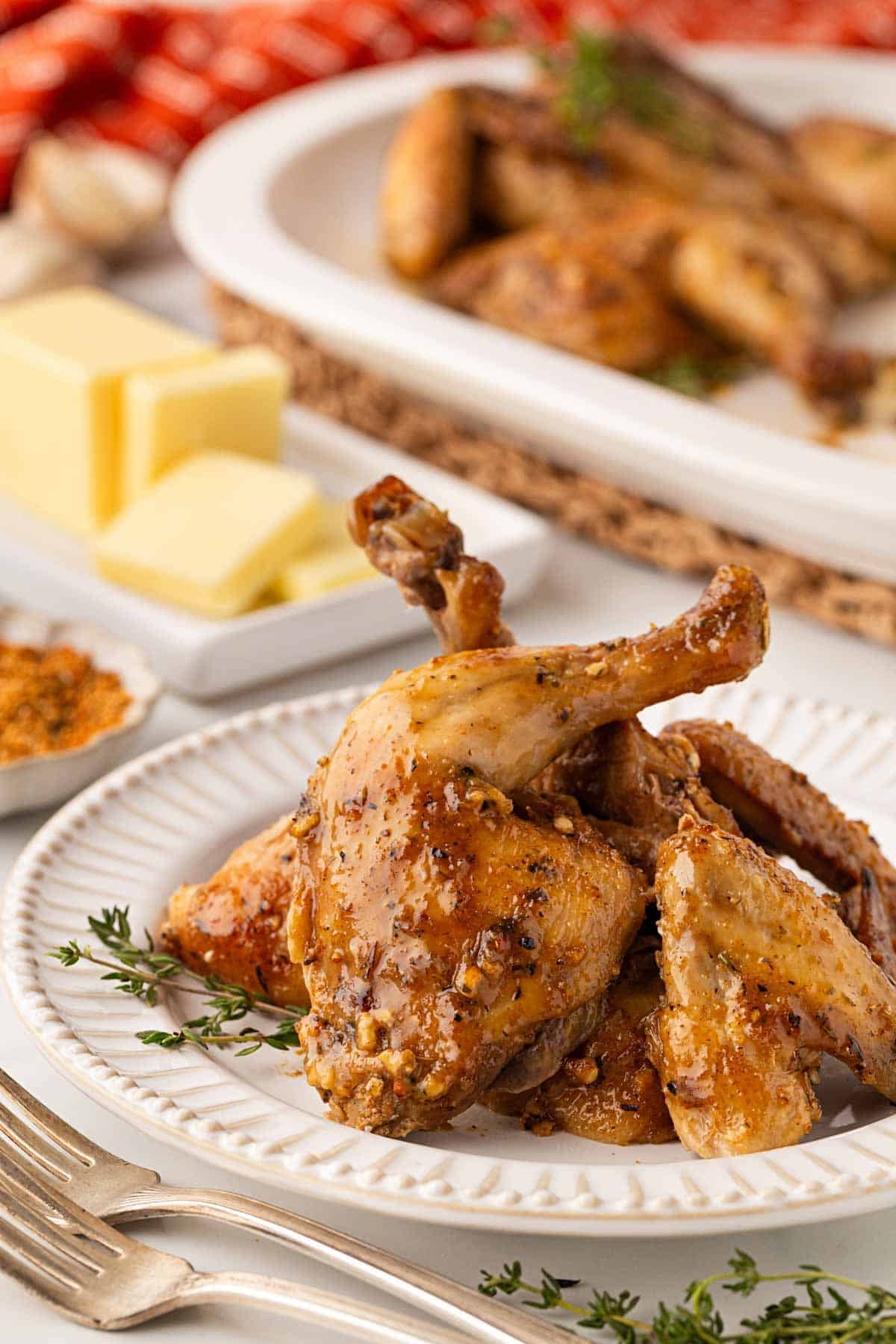 Closeup of roasted Cornish hens on a white plate with fresh thyme, butter, and another platter in the background