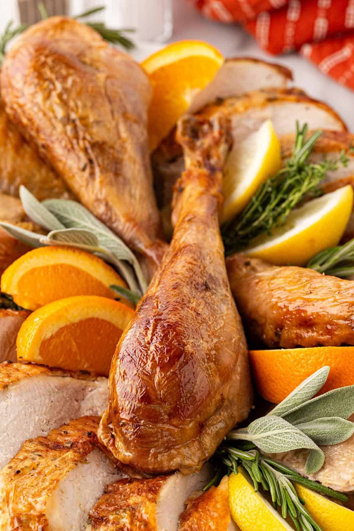 Closeup of golden roasted turkey drumsticks and sliced breast meat garnished with citrus wedges and fresh herbs