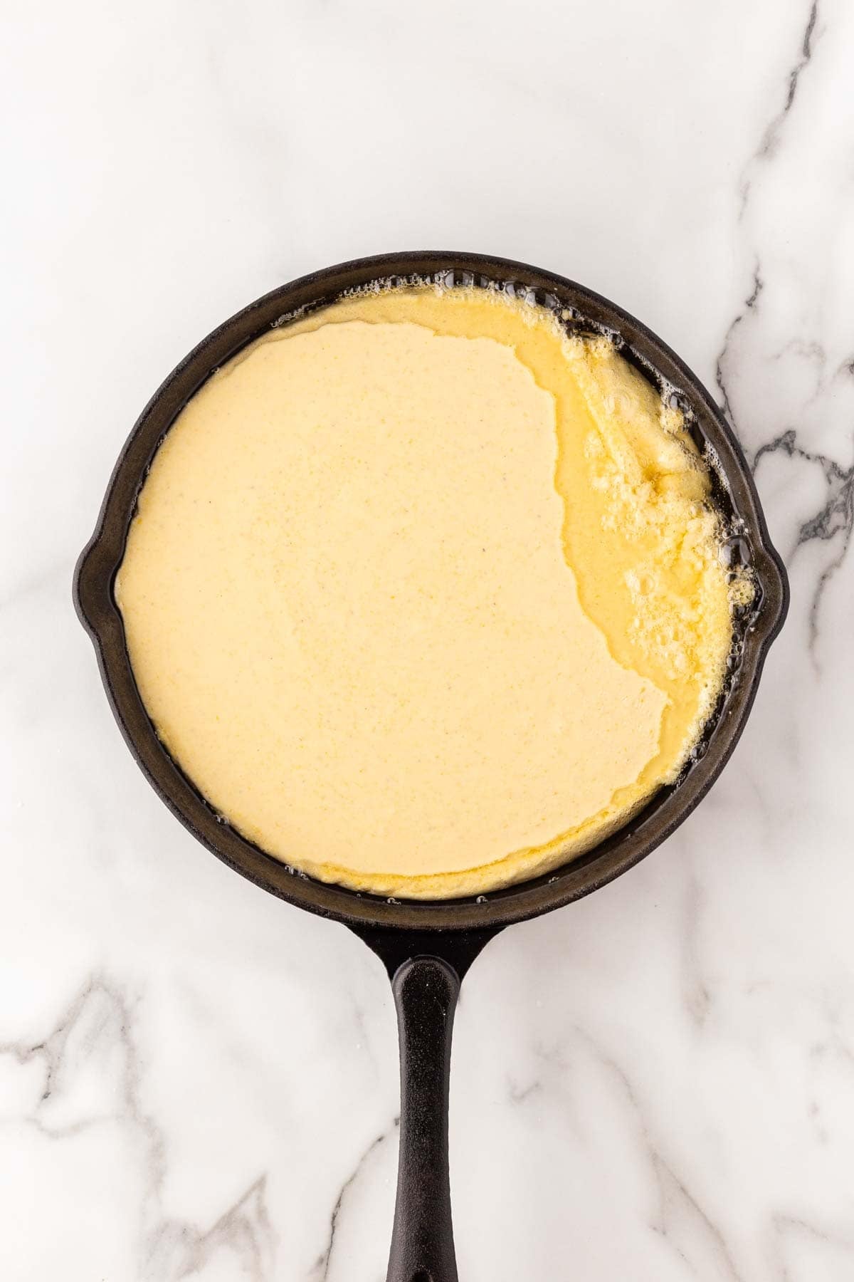 Cornbread batter poured into a hot cast-iron skillet with bubbling oil around the edges