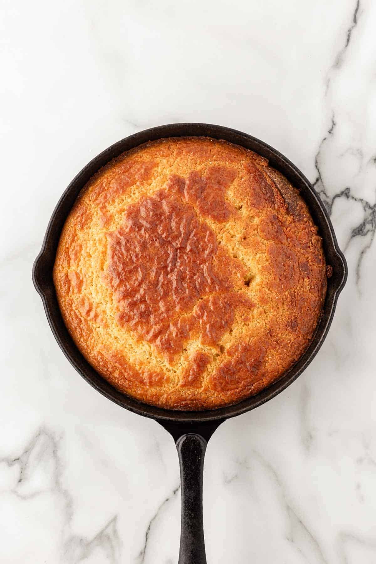 Freshly baked golden brown cornbread in a black cast-iron skillet on a white marble countertop