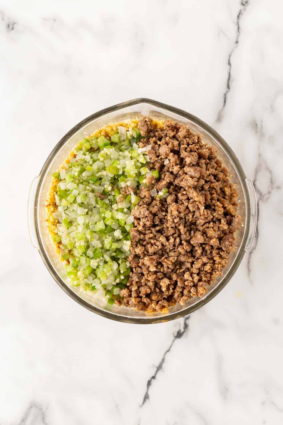 Cooked sage sausage and sautéed vegetables added to crumbled cornbread in a large glass bowl