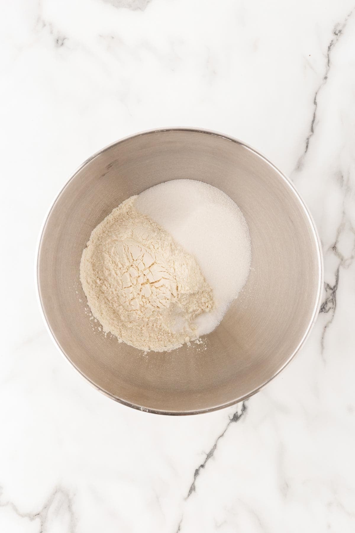 Flour and granulated sugar in a metal mixing bowl for cinnamon roll dough