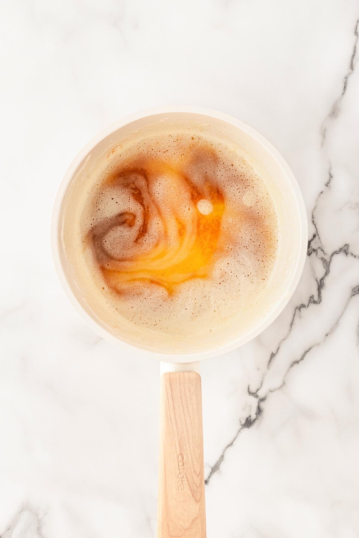 Browned butter with golden foam swirling in a saucepan on a marble surface