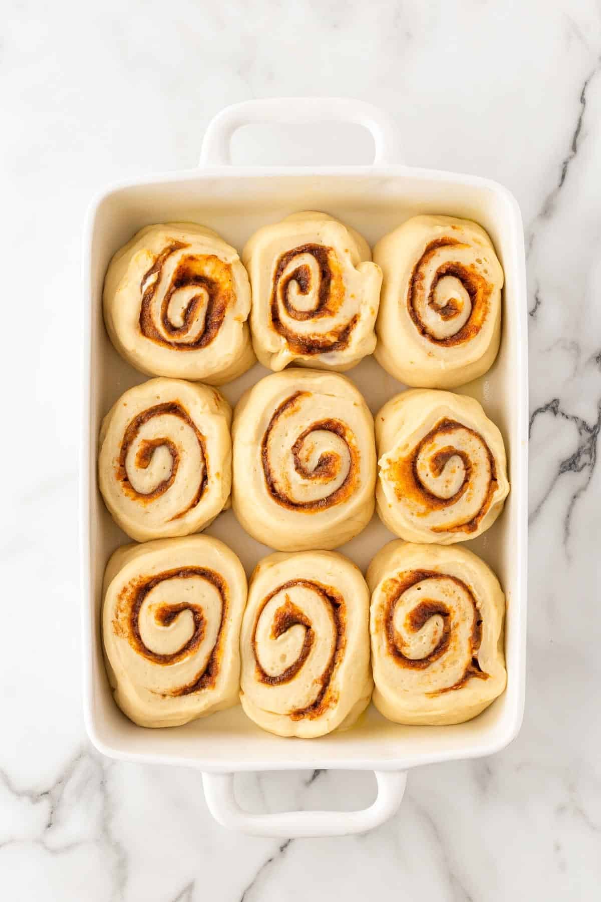 Nine unbaked sweet potato pie cinnamon rolls arranged in a baking dish