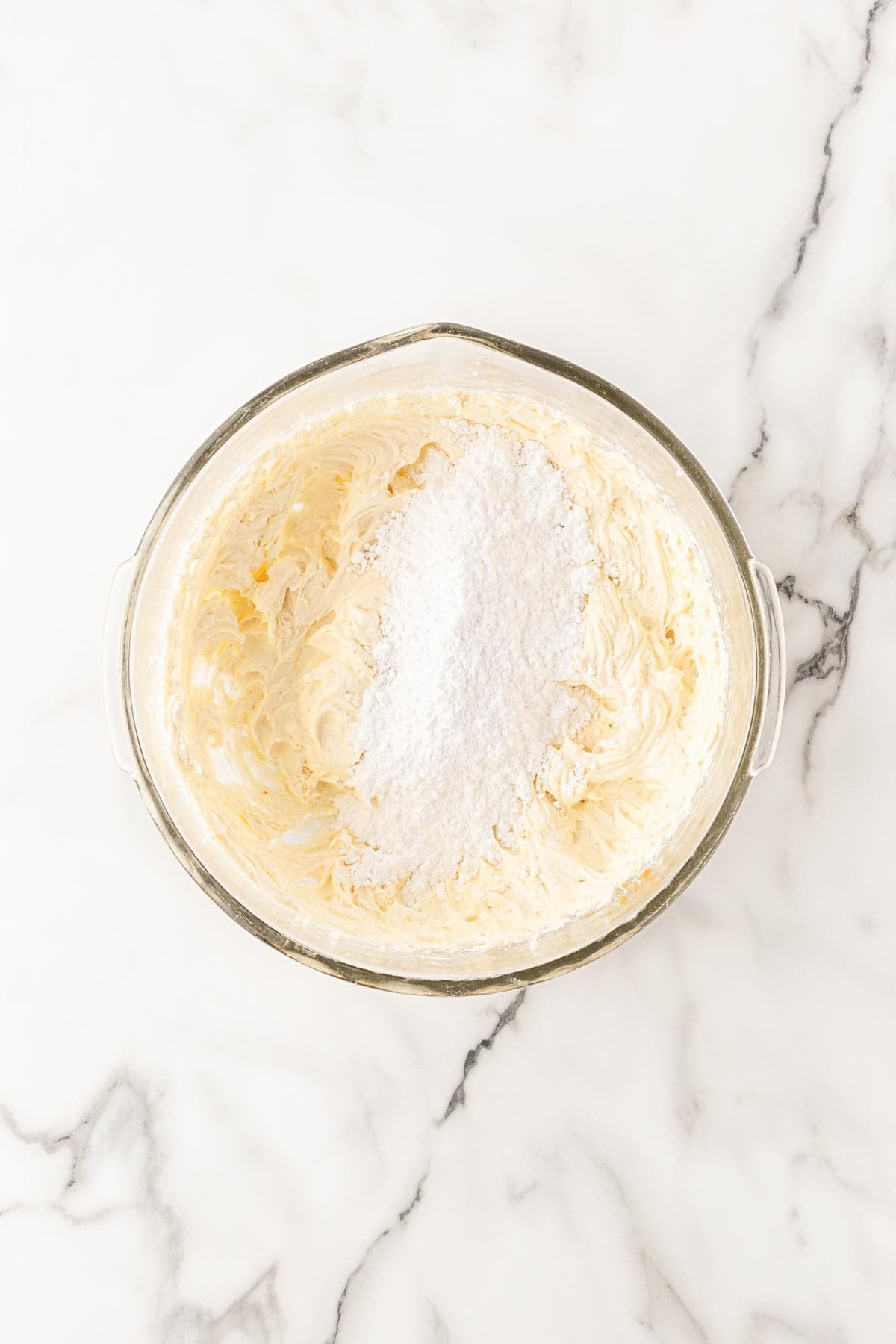Brown butter and cream cheese frosting mixture topped with powdered sugar in a glass bowl