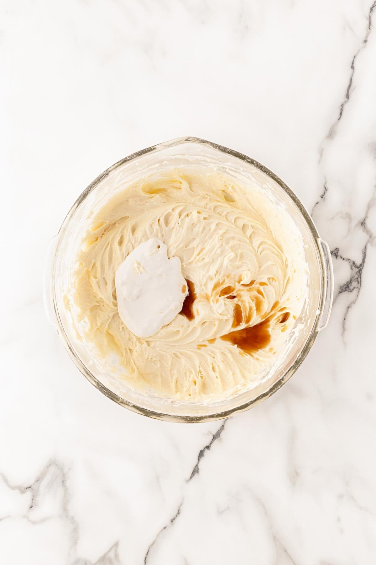 Cream cheese frosting being mixed with marshmallow fluff and vanilla in a glass bowl