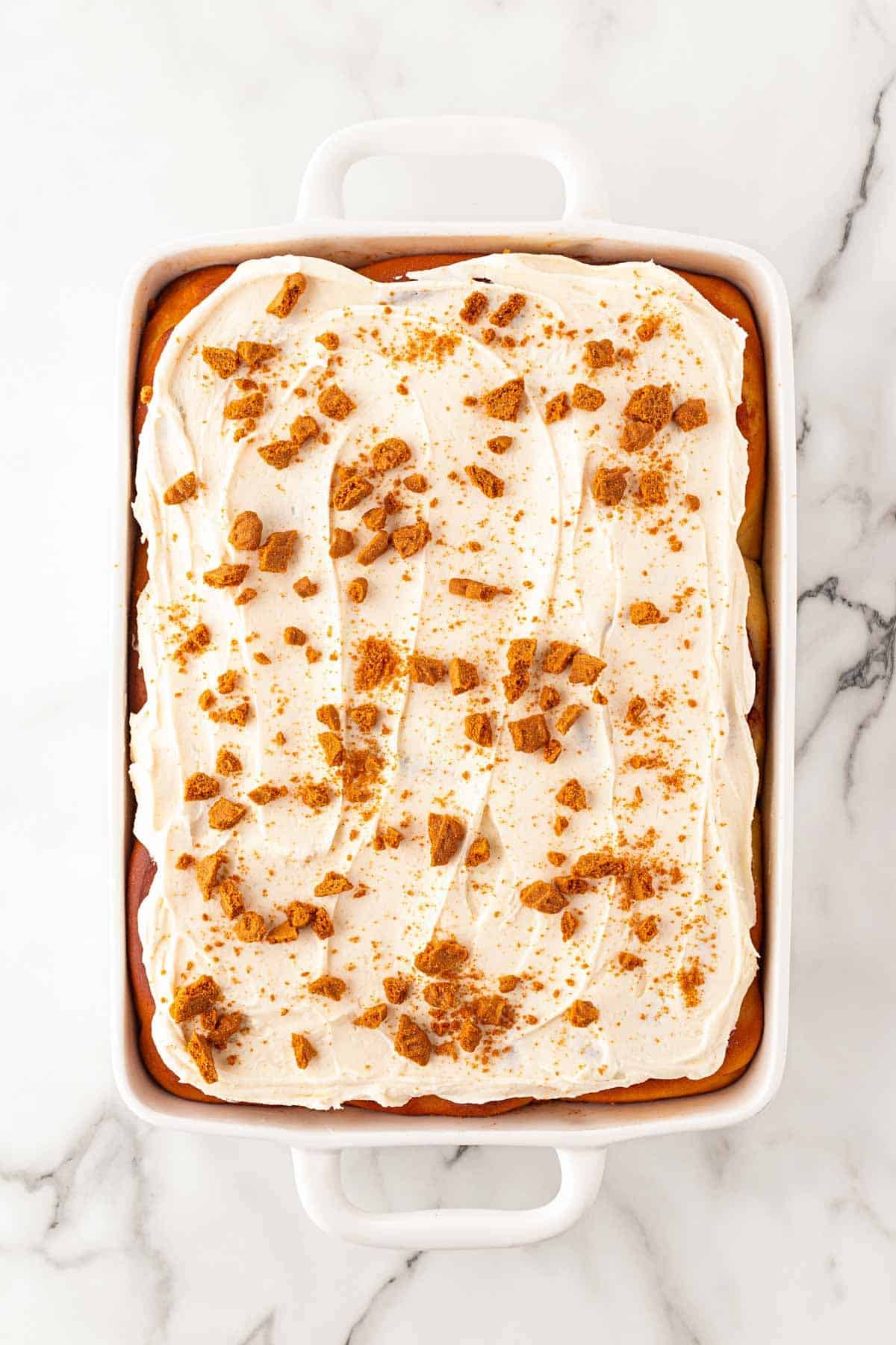 Sweet potato pie cinnamon rolls topped with cream cheese frosting and cookie crumbles in a baking dish