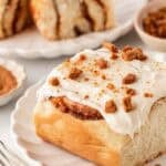 Sweet potato pie cinnamon roll topped with cream cheese frosting and cookie crumbles on a white plate
