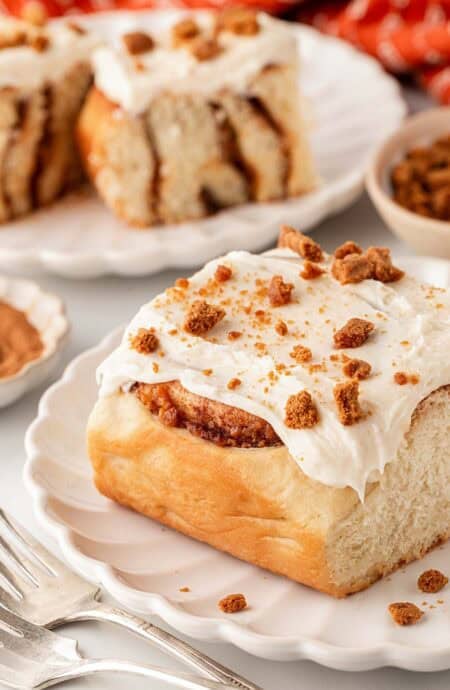 Sweet potato pie cinnamon roll topped with cream cheese frosting and cookie crumbles on a white plate