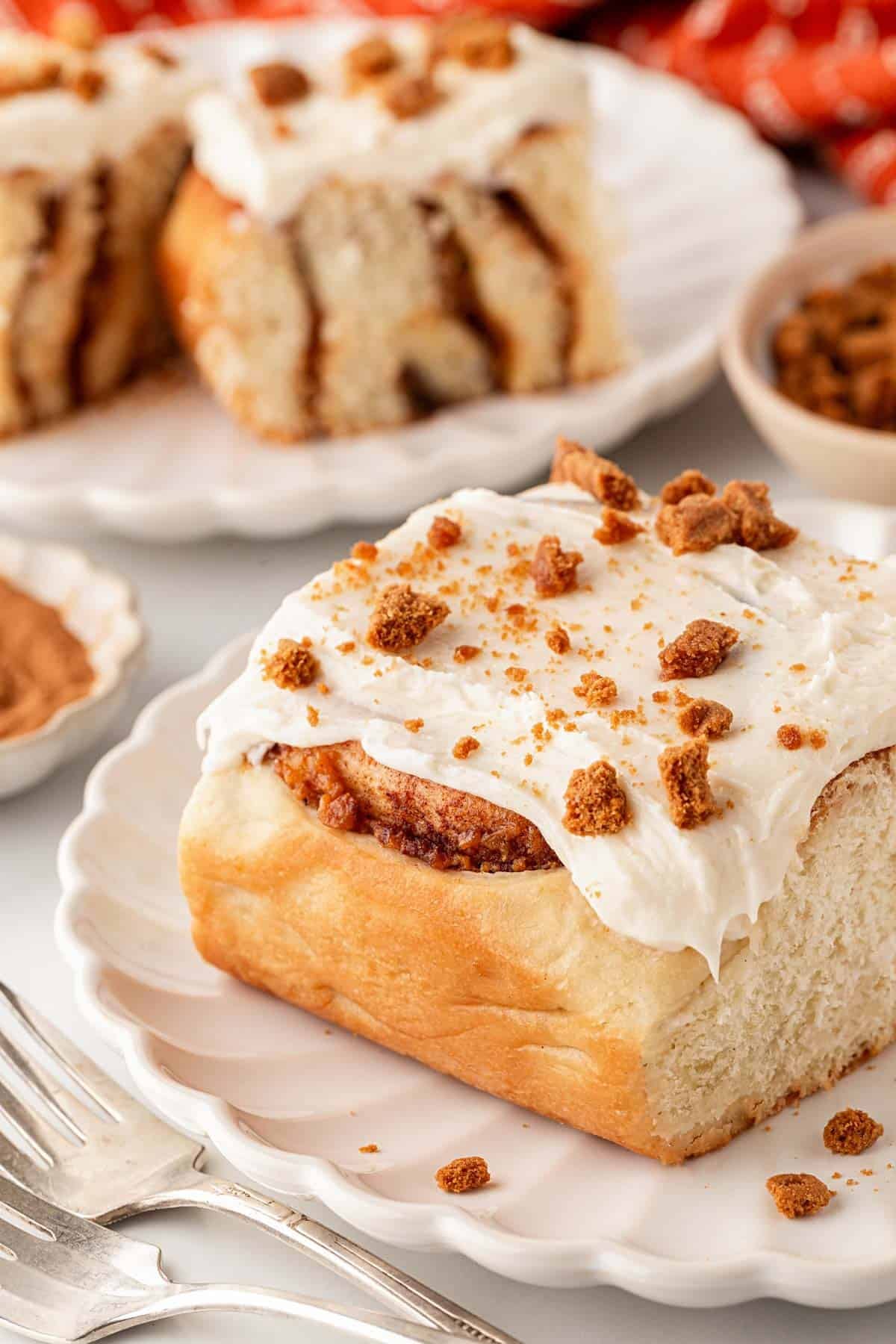Sweet potato pie cinnamon roll topped with cream cheese frosting and cookie crumbles on a white plate