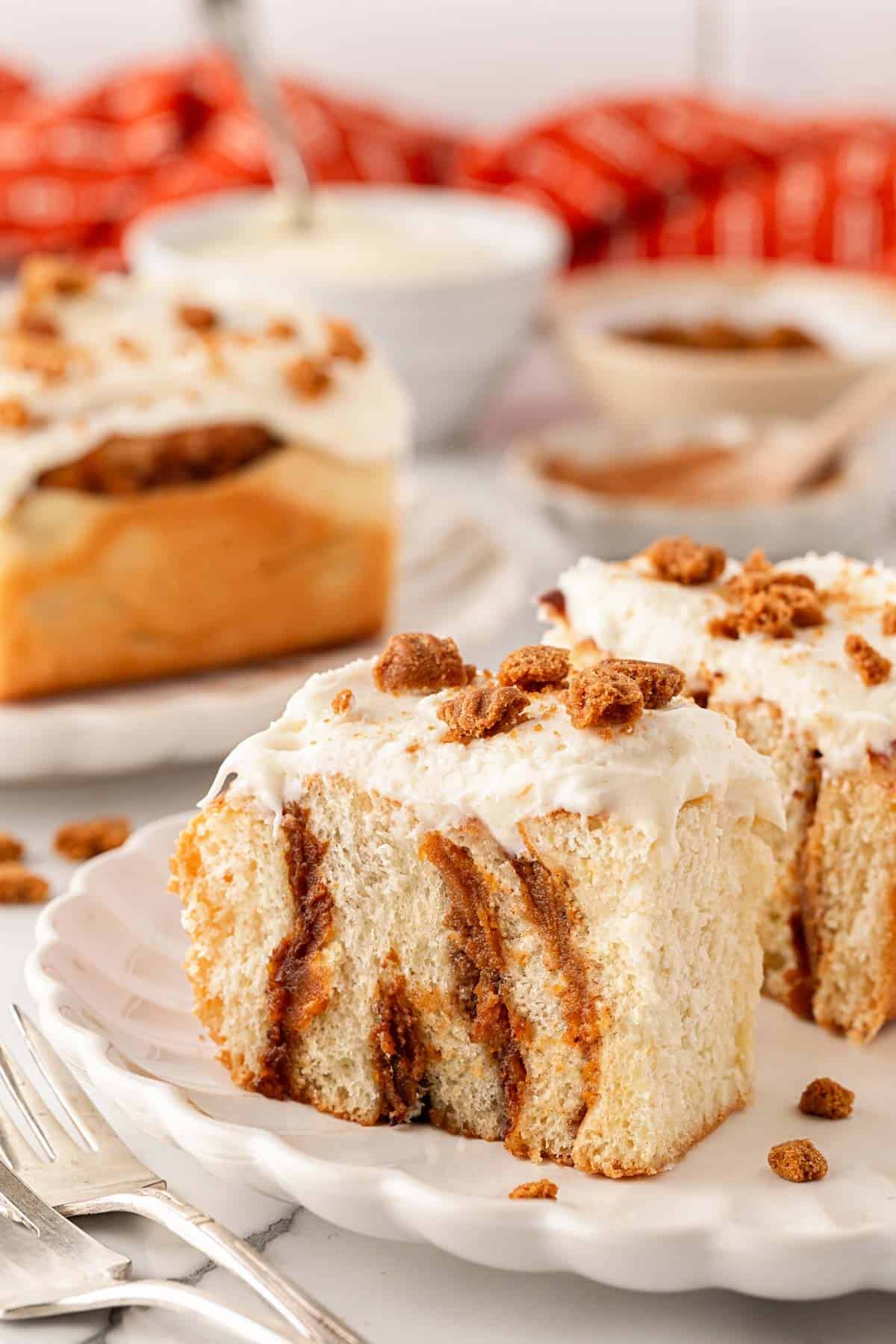 Slice of sweet potato pie cinnamon roll topped with cream cheese frosting and cookie crumbles on a white plate